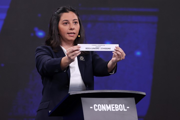 La representante de Conmebol Luciana Antunes sostiene la papeleta que anuncia el enfrentamiento entre Boca Juniors y O'Higgins (EFE).